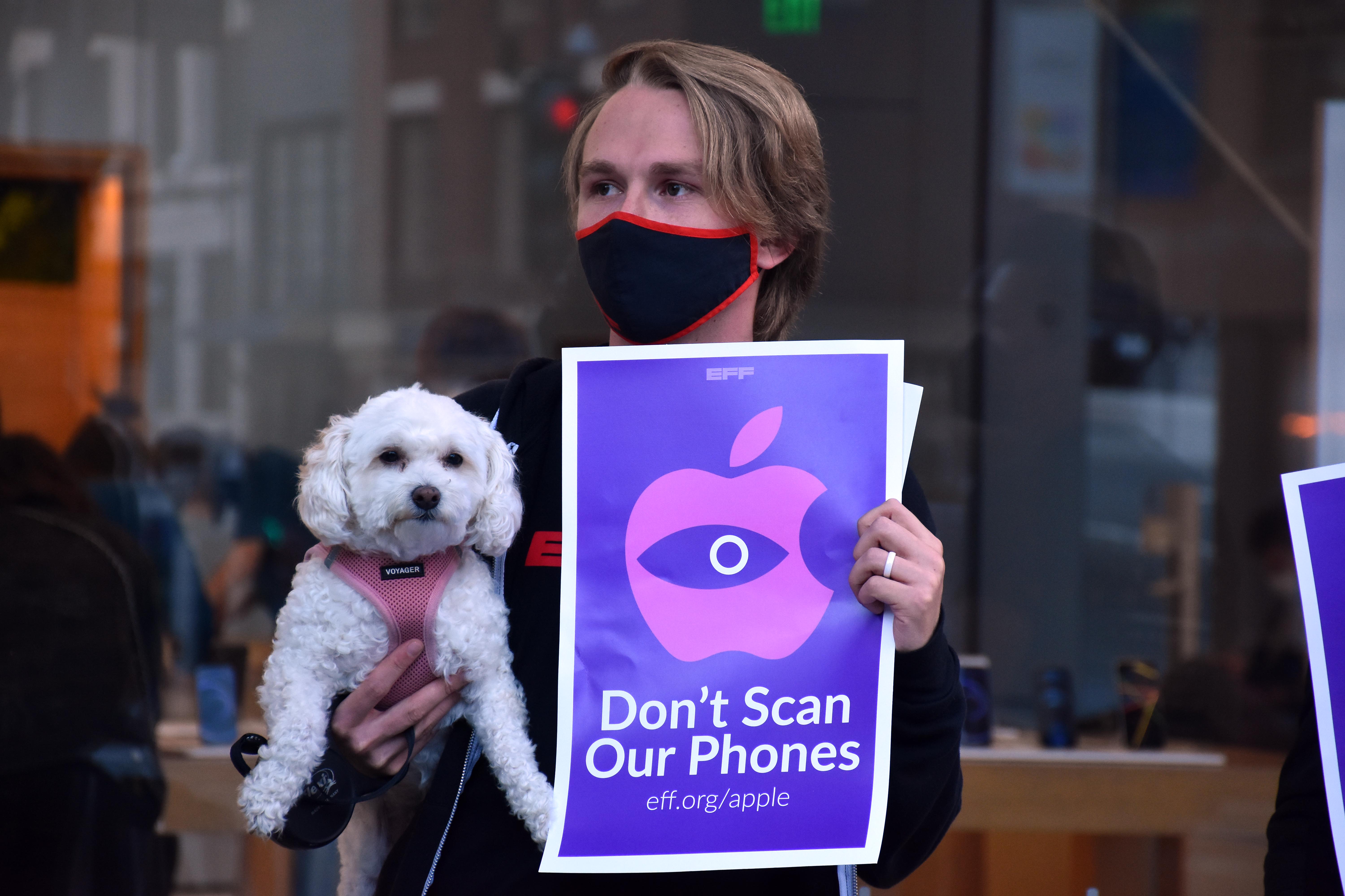 a man holds a poodle and a sign reading dont scan our phones