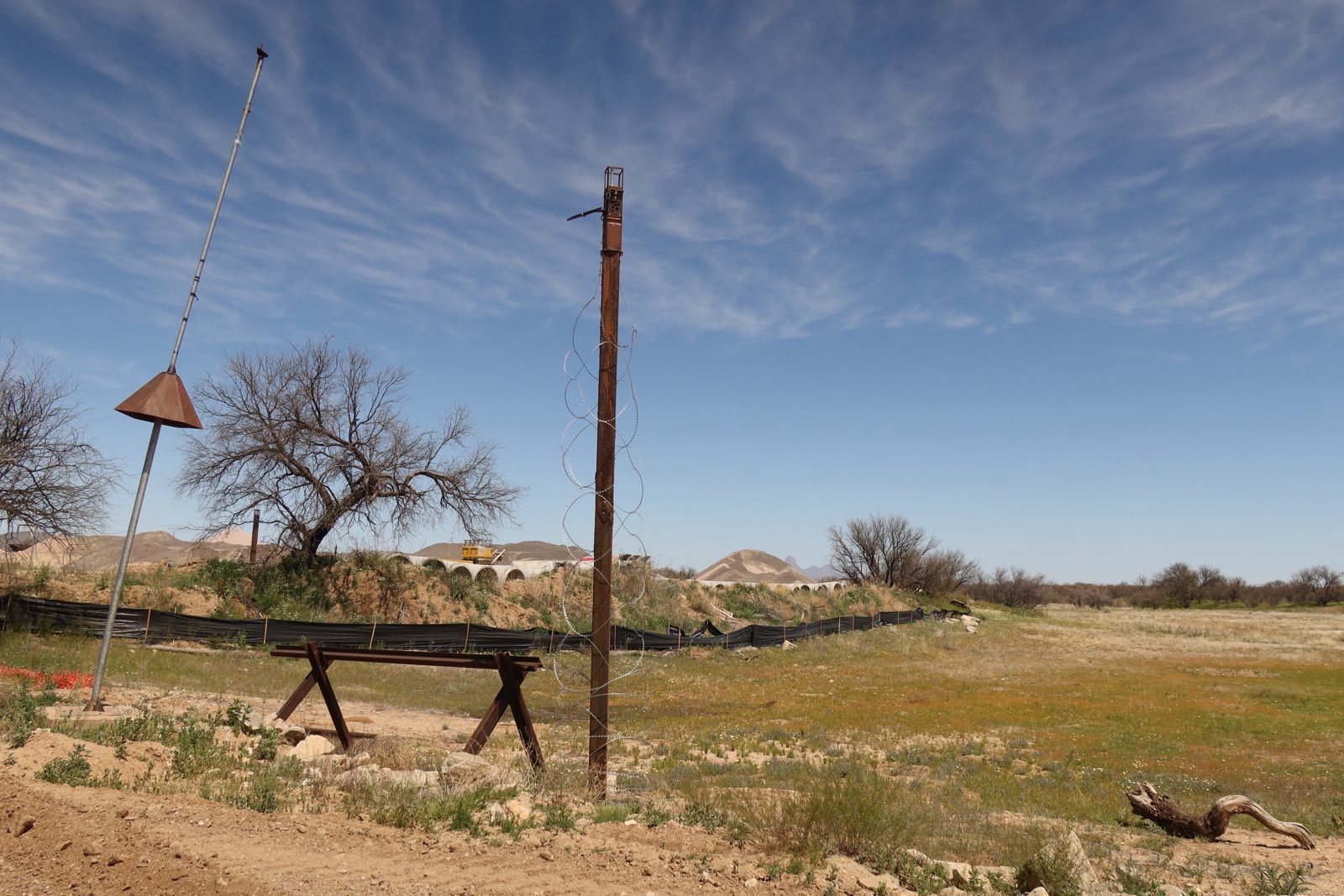 A desert scene with a rust-colored pole surrounded by razor wire. 