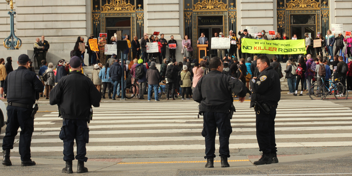 police look over a protest on the San Francisco city hall steps rallying against killer robots