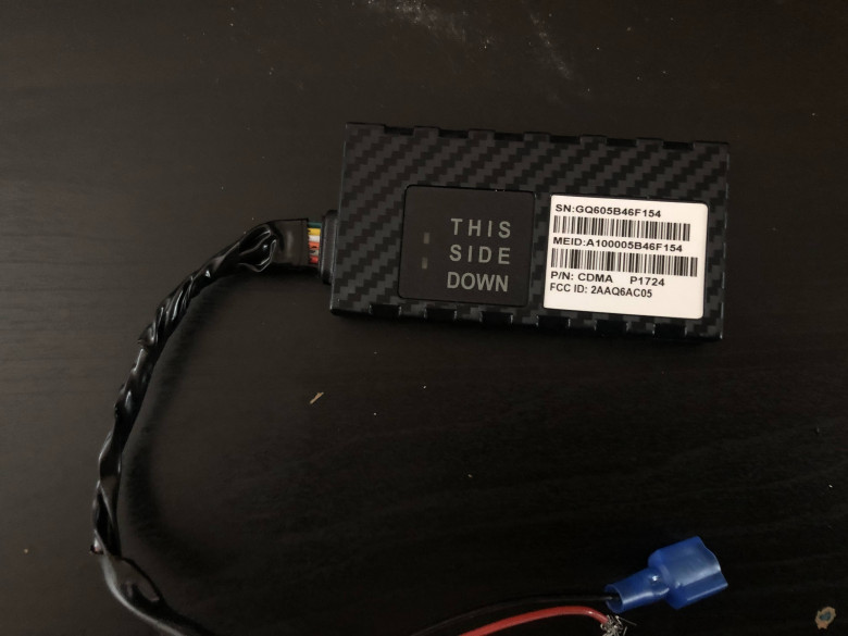 A GPS tracker found in a car. The front reads "this side down." There are three barcodes and wires coming out of the end.