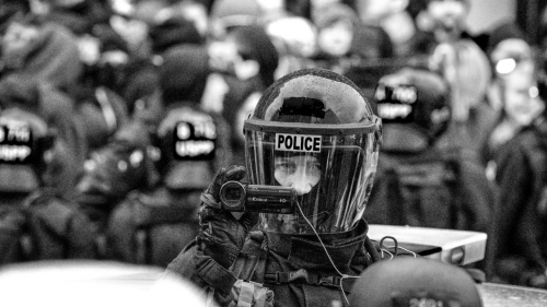 A riot police officer pointing a videocamera at the photographer.